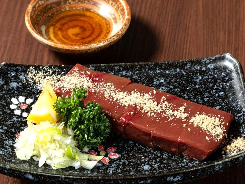 黒い長皿に盛った厚切りレバーとごま・薬味